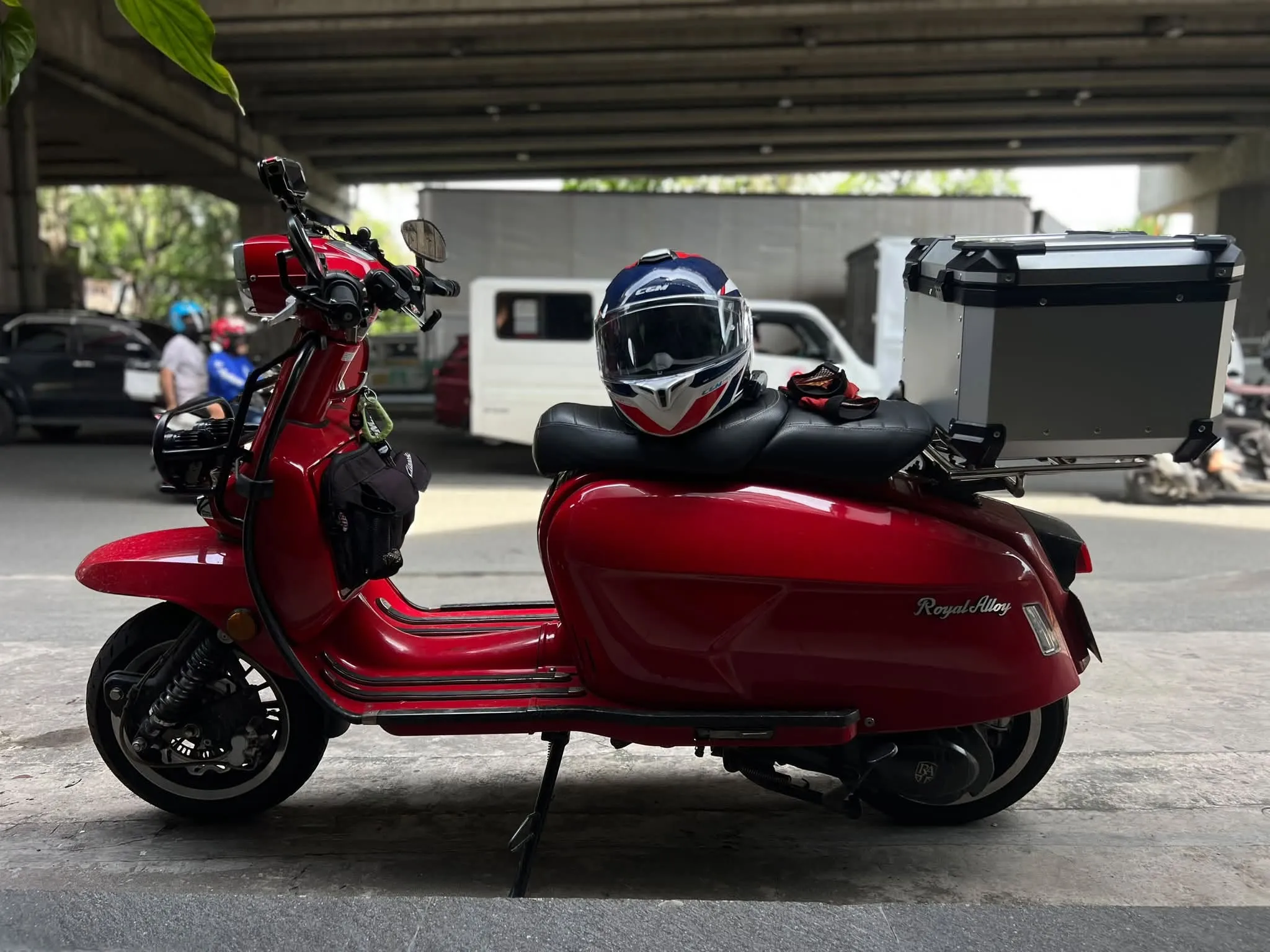 CGM Italia modular helmet resting on a Royal Alloy GP180 with a 55L X-Land top box, parked under a Manila overpass